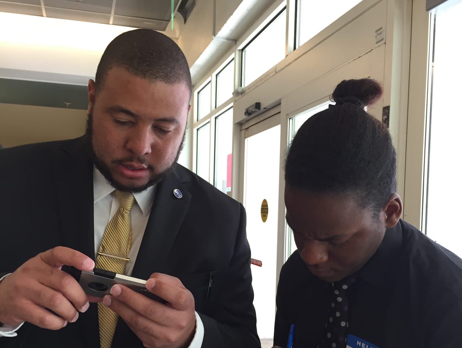 A man in a suit and a student side by side, both focused on their work