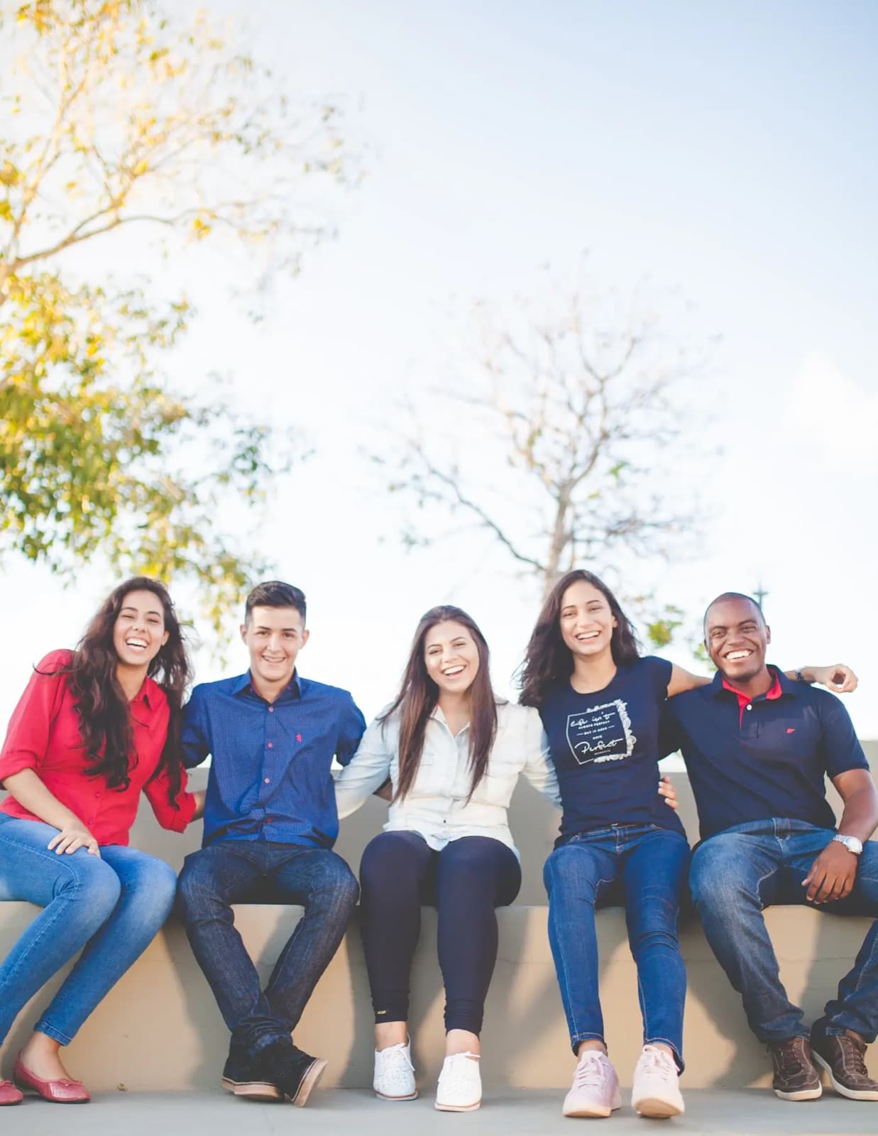 Five smiling students sitting together outdoors