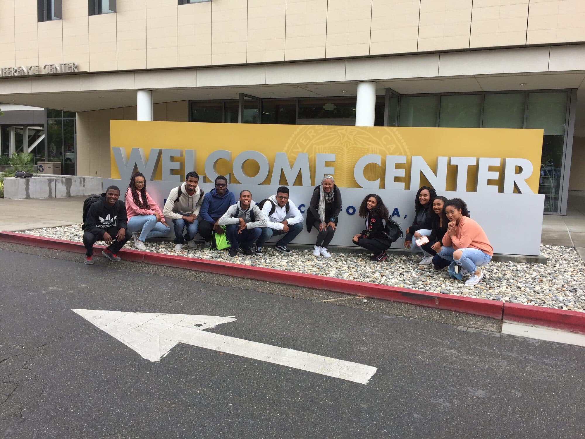 A group of scholars gathered at a campus Welcome Center sign